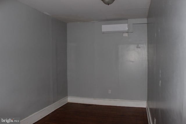 empty room with a wall unit AC, baseboards, and dark wood-type flooring