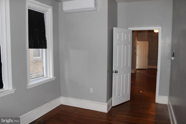 unfurnished room with dark wood finished floors, a wall mounted AC, and baseboards