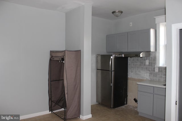 kitchen with baseboards, gray cabinets, freestanding refrigerator, decorative backsplash, and light countertops