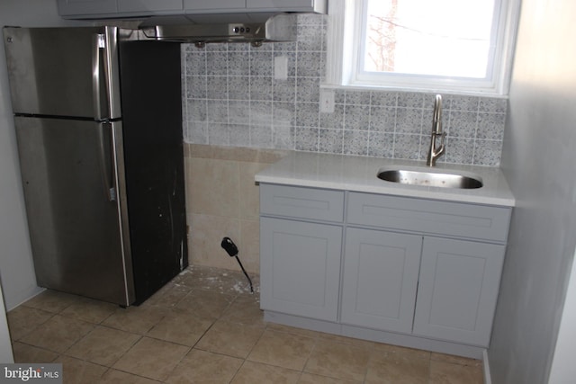 kitchen with light tile patterned floors, light countertops, freestanding refrigerator, and a sink