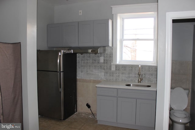 kitchen with light tile patterned flooring, freestanding refrigerator, a sink, light countertops, and tile walls