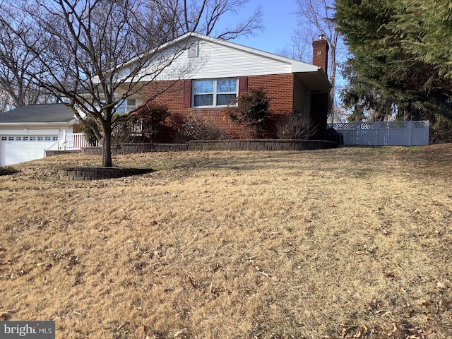 view of side of property with a garage, fence, brick siding, and a chimney