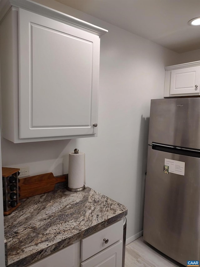 kitchen with baseboards, light stone countertops, freestanding refrigerator, light wood-style floors, and white cabinets