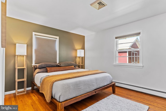 bedroom with visible vents, baseboard heating, light wood-type flooring, and baseboards