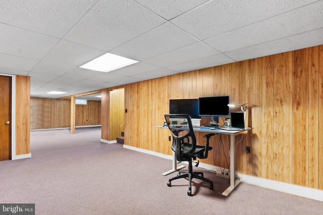 office space with a drop ceiling, carpet, and wood walls