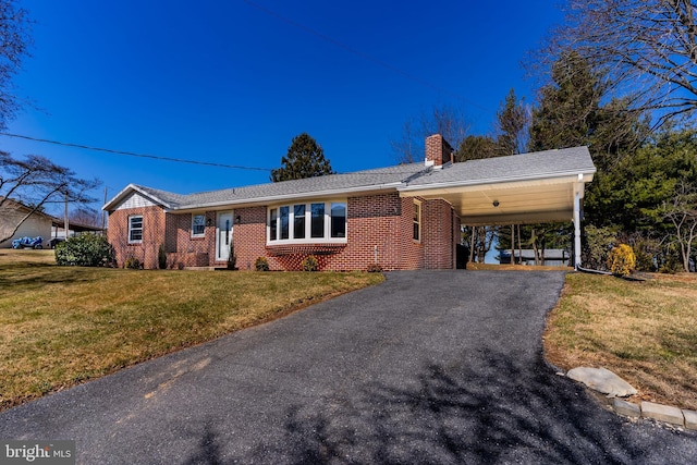 ranch-style home with a front yard, driveway, a chimney, a carport, and brick siding