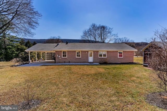 back of property with brick siding, an attached carport, a lawn, a patio area, and driveway