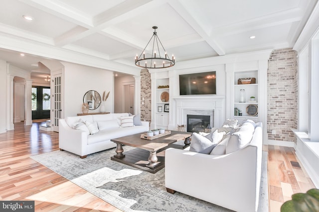 living area featuring decorative columns, built in shelves, light wood-style floors, and beam ceiling