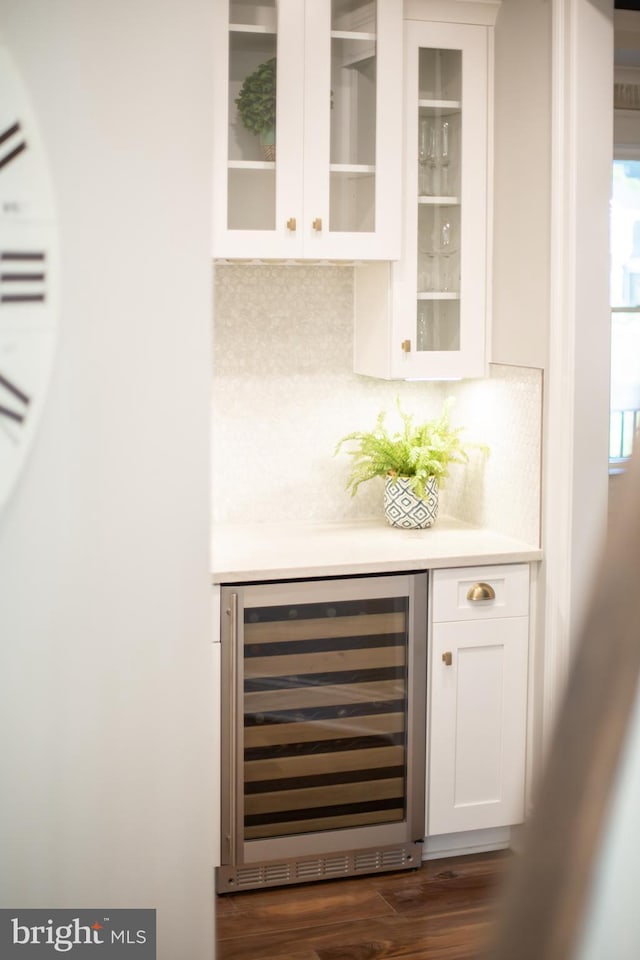 bar featuring wine cooler, a bar, dark wood-style flooring, and tasteful backsplash