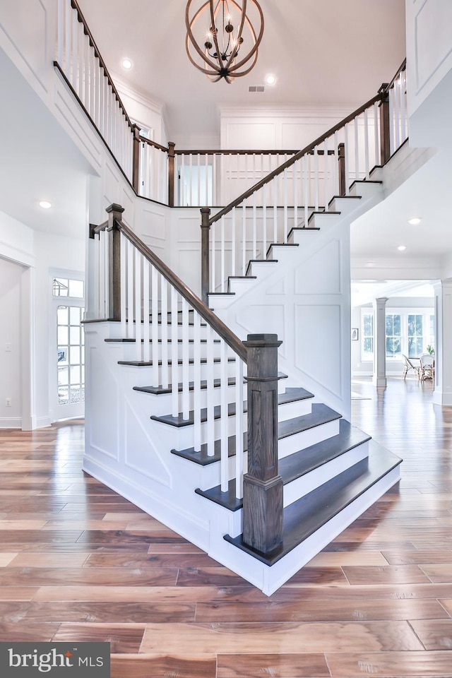 staircase with wood finished floors, decorative columns, recessed lighting, a decorative wall, and a chandelier