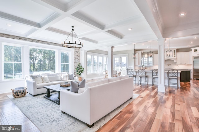 living area featuring decorative columns, beam ceiling, light wood-style floors, and an inviting chandelier