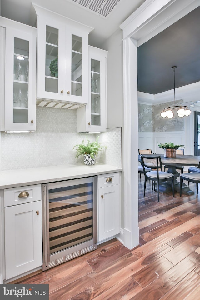 bar with a notable chandelier, beverage cooler, wood finished floors, a bar, and hanging light fixtures