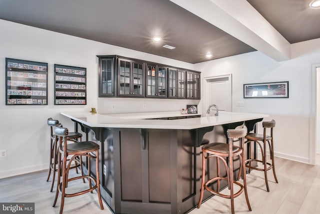 bar featuring light wood finished floors, indoor wet bar, baseboards, and a sink