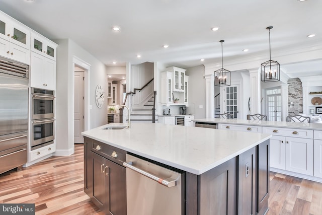 kitchen with a kitchen island with sink, decorative columns, appliances with stainless steel finishes, white cabinets, and a sink