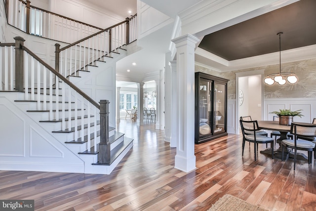 interior space featuring a decorative wall, wood finished floors, ornate columns, and ornamental molding