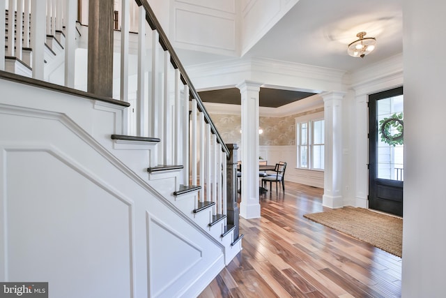 foyer featuring crown molding, stairway, wainscoting, wood finished floors, and ornate columns