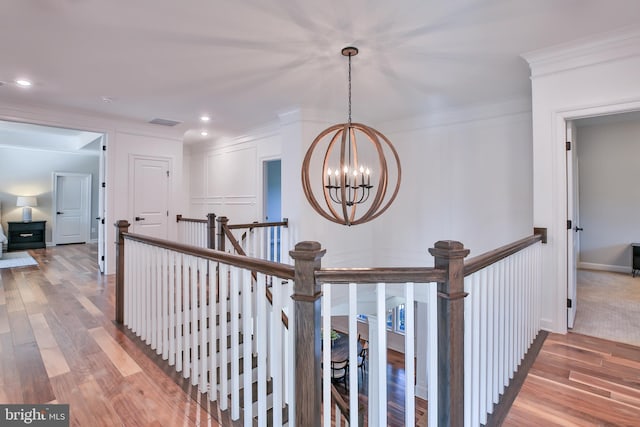 hallway with crown molding, wood finished floors, an upstairs landing, and a chandelier