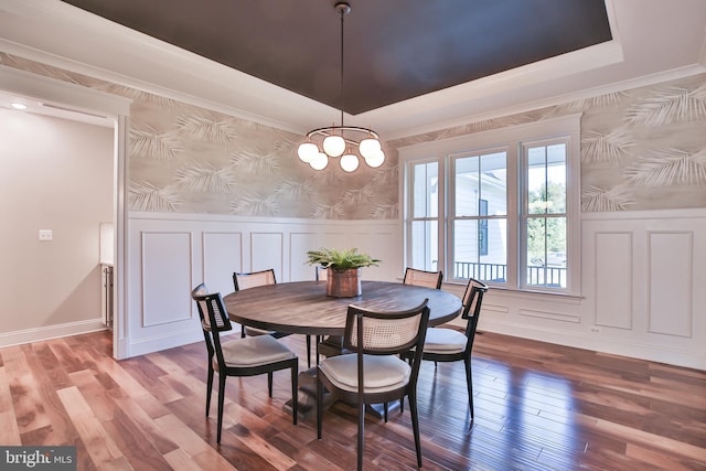 dining area featuring wood finished floors, a wainscoted wall, wallpapered walls, a tray ceiling, and a decorative wall