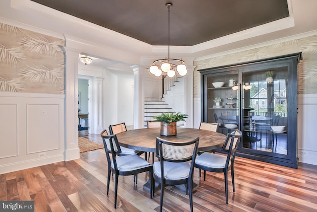 dining space with stairs, a raised ceiling, decorative columns, and wood finished floors