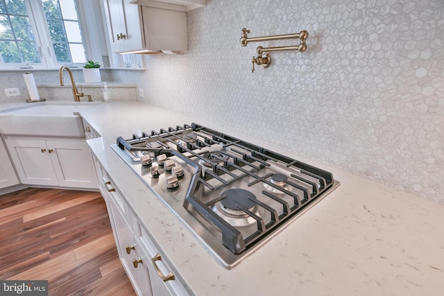 room details with stainless steel gas stovetop, light stone counters, wood finished floors, white cabinets, and a sink