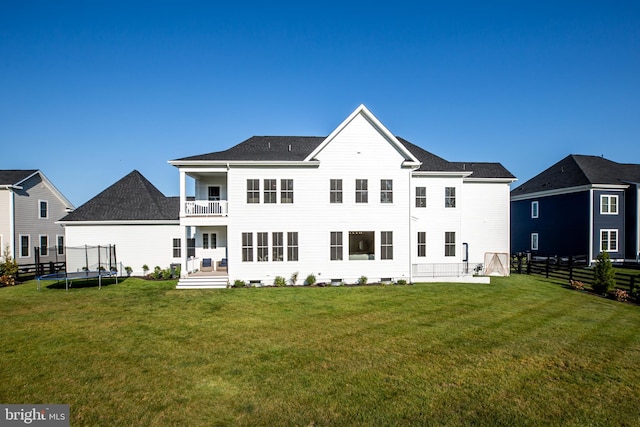 back of property with fence, a trampoline, a balcony, and a lawn