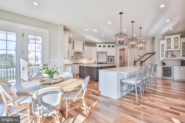 kitchen featuring light wood-style flooring, beverage cooler, a spacious island, appliances with stainless steel finishes, and light countertops