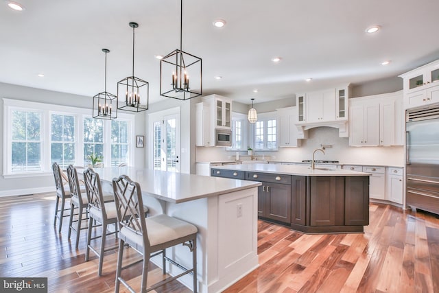 kitchen with light countertops, a center island with sink, built in appliances, and a sink