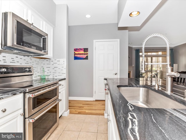 kitchen featuring a sink, stainless steel appliances, white cabinets, light tile patterned floors, and decorative backsplash