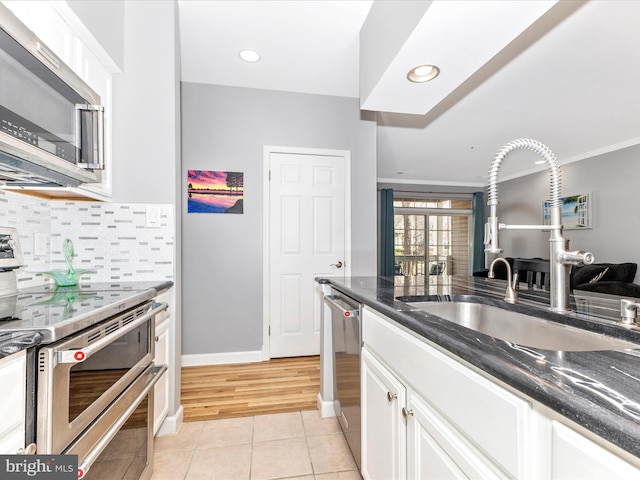 kitchen featuring a sink, stainless steel appliances, white cabinets, light tile patterned floors, and decorative backsplash