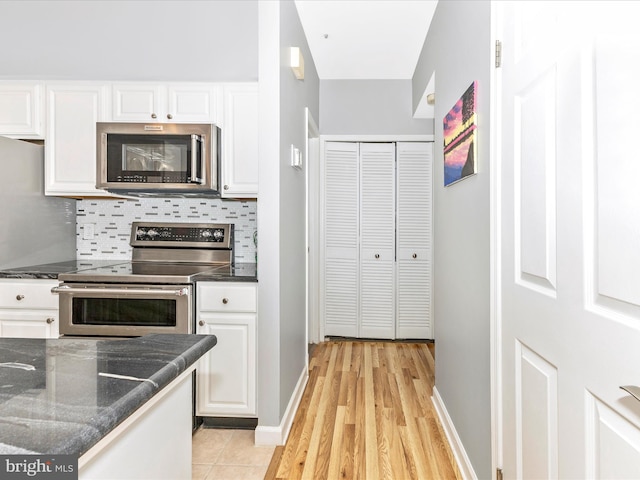 kitchen with baseboards, decorative backsplash, dark stone countertops, stainless steel appliances, and white cabinetry