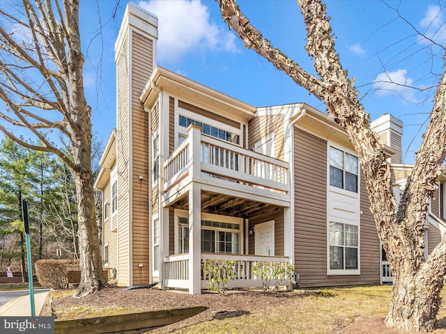 view of front of house featuring a balcony, covered porch, and a chimney