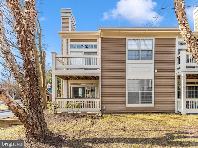 exterior space featuring a front lawn, a balcony, and a chimney