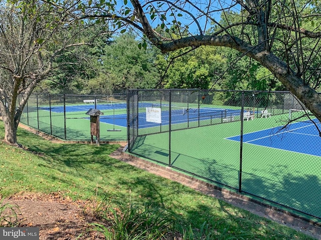 view of tennis court with a yard and fence