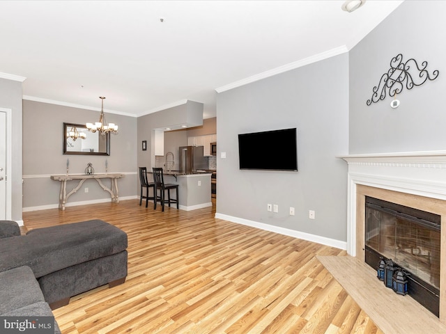 living room with crown molding, a notable chandelier, light wood-style floors, and baseboards