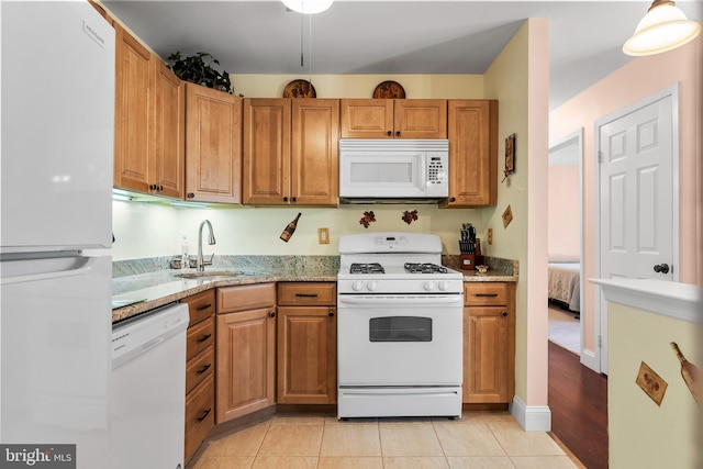 kitchen with a sink, white appliances, brown cabinetry, and light tile patterned floors