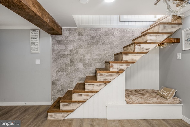 stairs with beamed ceiling, baseboards, wood finished floors, and crown molding