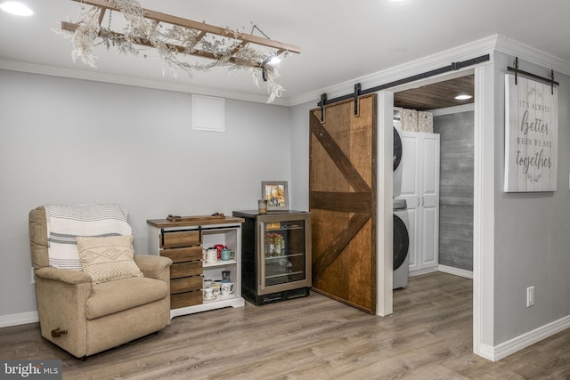 living area with ornamental molding, wood finished floors, a barn door, stacked washer / dryer, and baseboards