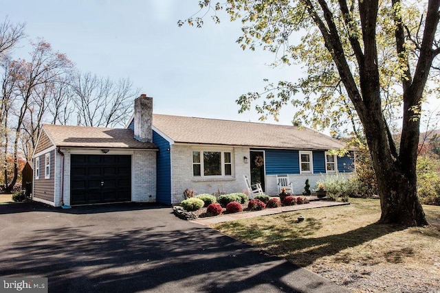 single story home featuring a garage, brick siding, a chimney, and aphalt driveway