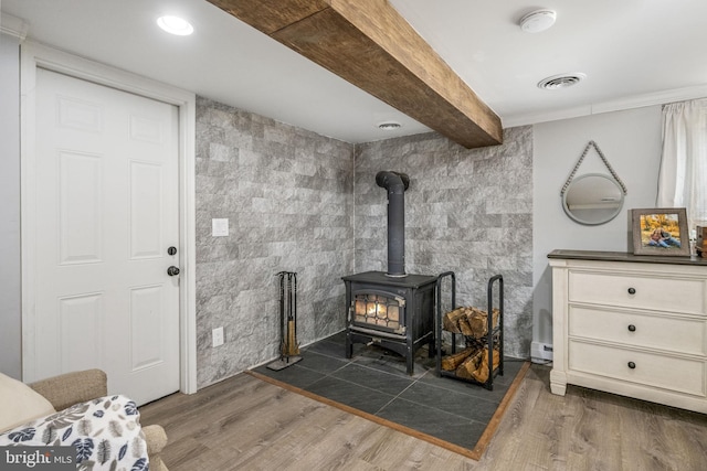 interior details with visible vents, beamed ceiling, a wood stove, and wood finished floors