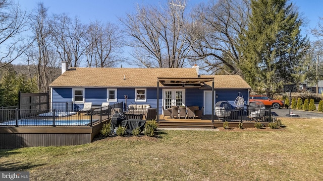 back of house featuring a wooden deck, a shingled roof, a chimney, french doors, and a lawn