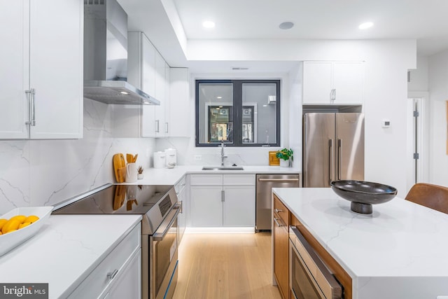 kitchen featuring light wood finished floors, a sink, stainless steel appliances, white cabinets, and wall chimney exhaust hood