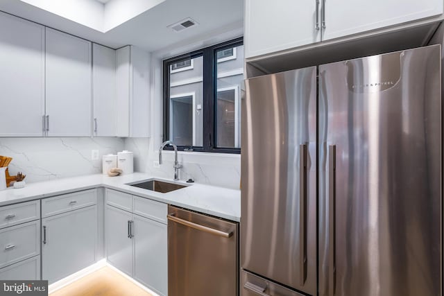 kitchen featuring visible vents, backsplash, light stone counters, stainless steel appliances, and a sink