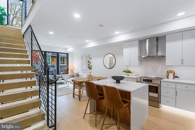 kitchen with light wood finished floors, a kitchen island, a breakfast bar, electric range, and wall chimney exhaust hood