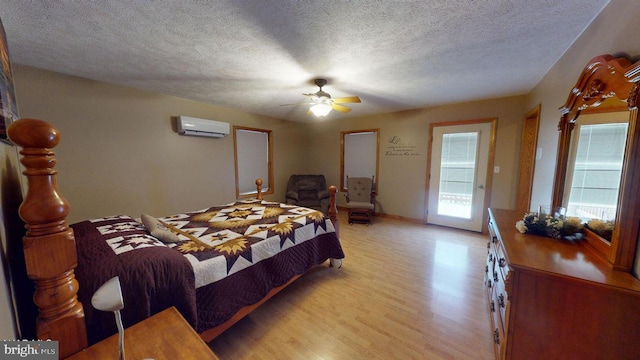 bedroom featuring baseboards, ceiling fan, an AC wall unit, light wood-style flooring, and a textured ceiling