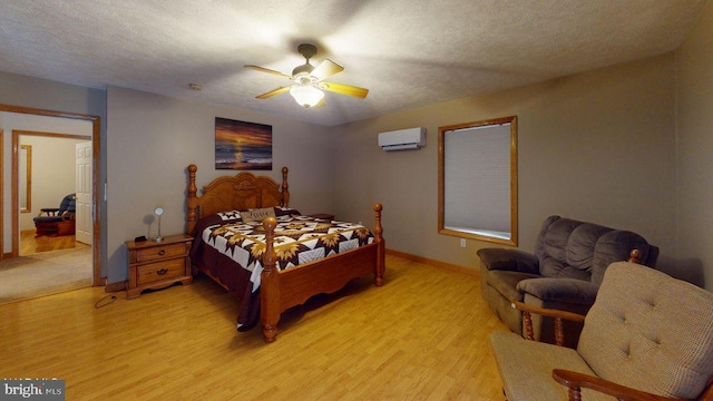 bedroom featuring a ceiling fan, baseboards, an AC wall unit, light wood-style floors, and a textured ceiling