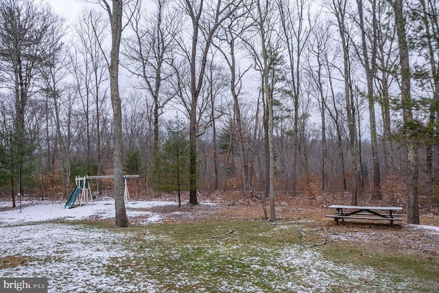 snowy yard featuring playground community and a wooded view