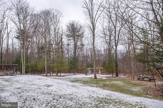 snowy yard featuring a view of trees and playground community