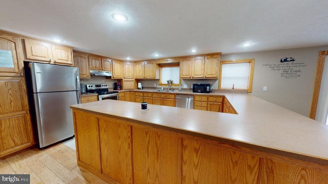 kitchen with a peninsula, recessed lighting, stainless steel appliances, light wood-style floors, and under cabinet range hood