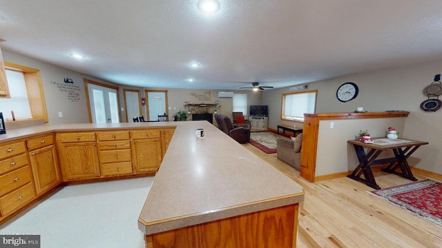 kitchen with light wood finished floors, a fireplace, light countertops, and a peninsula