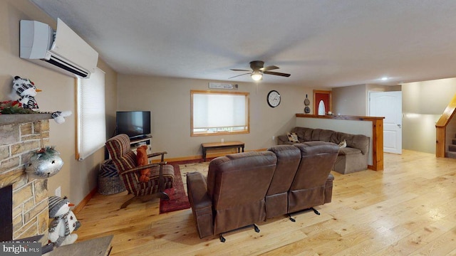 living room with baseboards, a fireplace, ceiling fan, an AC wall unit, and light wood-style floors